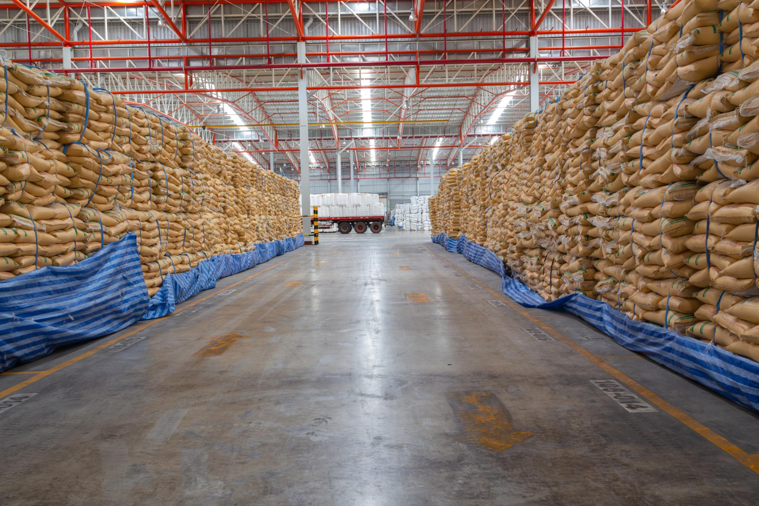 Interior de un gran almacén con altas pilas de sacos de pienso organizadas en hileras